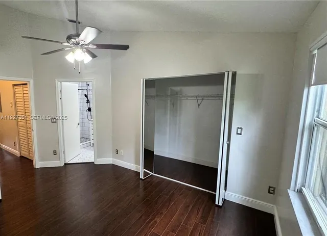 an empty room with wooden floor a ceiling fan and windows