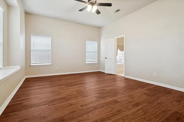 an empty room with wooden floor chandelier fan and windows