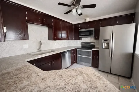 a kitchen with stainless steel appliances granite countertop a refrigerator a sink a stove top oven and a counter space