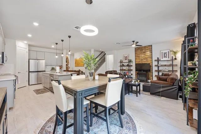 a dining area with stainless steel appliances kitchen island granite countertop a dining table chairs and a refrigerator