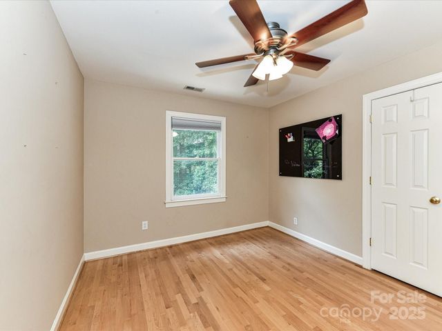 an empty room with wooden floor chandelier fan and windows