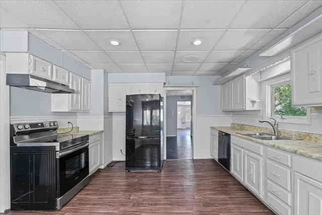 a kitchen with stainless steel appliances granite countertop a stove a sink dishwasher a refrigerator and white cabinets with wooden floor