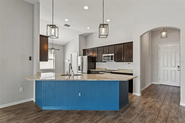 a view of kitchen with kitchen island stainless steel appliances sink stove refrigerator and wooden floor