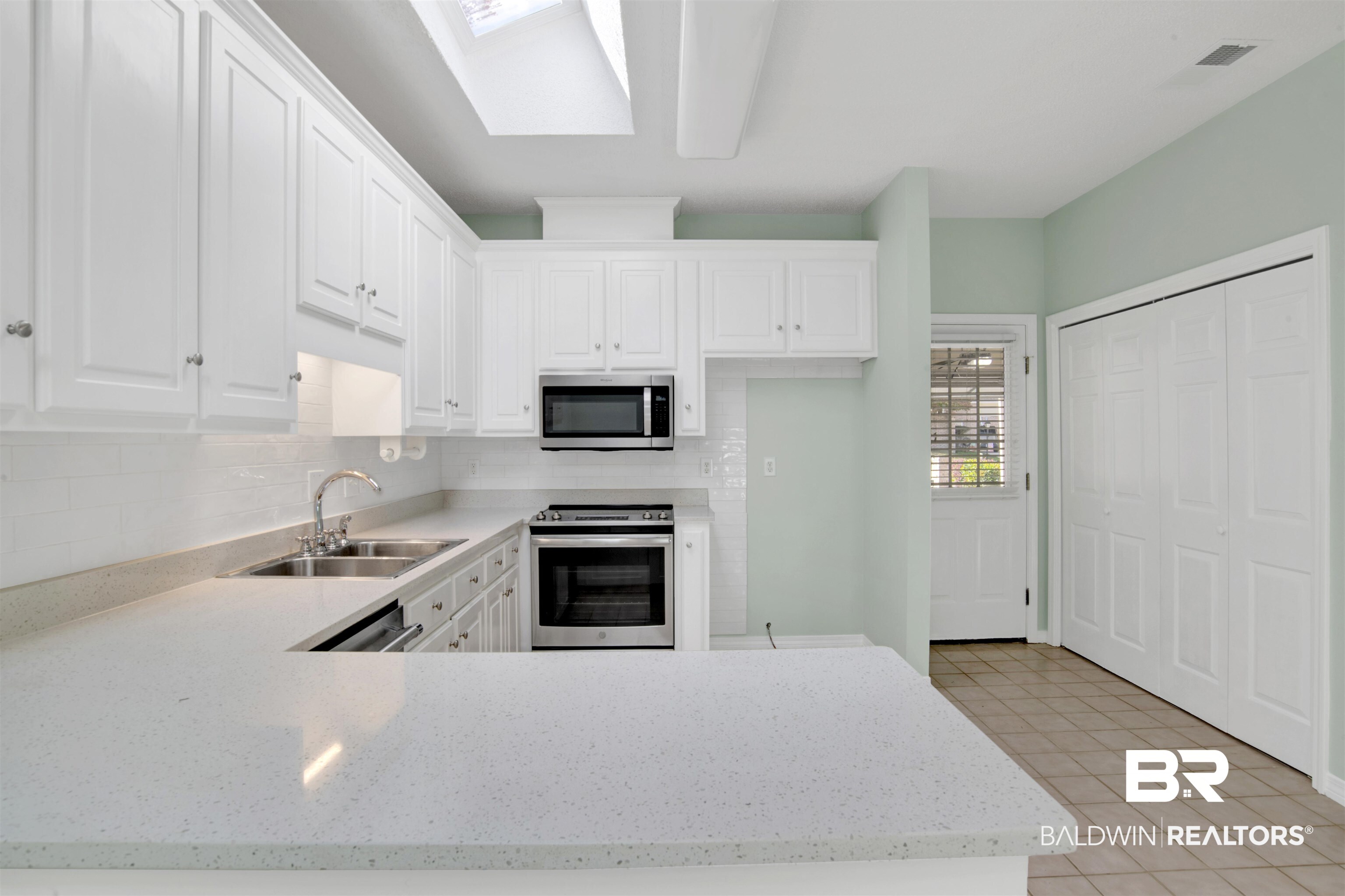 125 Woodruff Court Mobile, AL 36608 - Photo 12 of 27 Kitchen featuring a skylight, sink, white cabinetry, stainless steel appliances, and light tile patterned floors