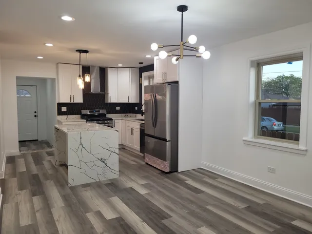 a kitchen with stainless steel appliances granite countertop a refrigerator a oven a sink dishwasher and white cabinets with wooden floor