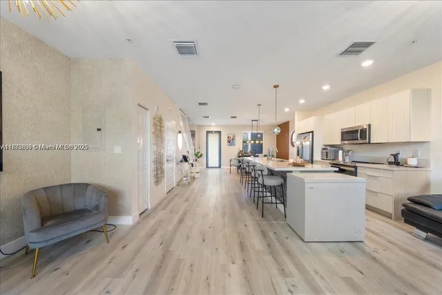 a living room with stainless steel appliances furniture wooden floor and a kitchen view