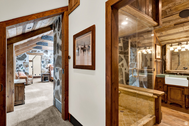 2983 East Ridgetop Road, Unit 27 Provo, UT 84604 - Photo 39 of 63 Elegant hallway showcasing rich wood-trimmed doorways and framed architectural details, leading to a spa-inspired bathroom featuring a walk-in shower with glass enclosure, warm wood cabinetry, and tile flooring