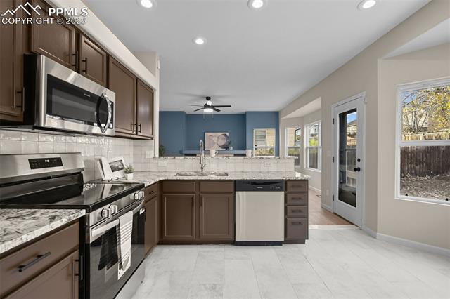 5428 Rondo Way Colorado Springs, CO 80911 - Photo 11 of 43 Kitchen with appliances with stainless steel finishes, dark brown cabinetry, backsplash, light stone countertops, and recessed lighting