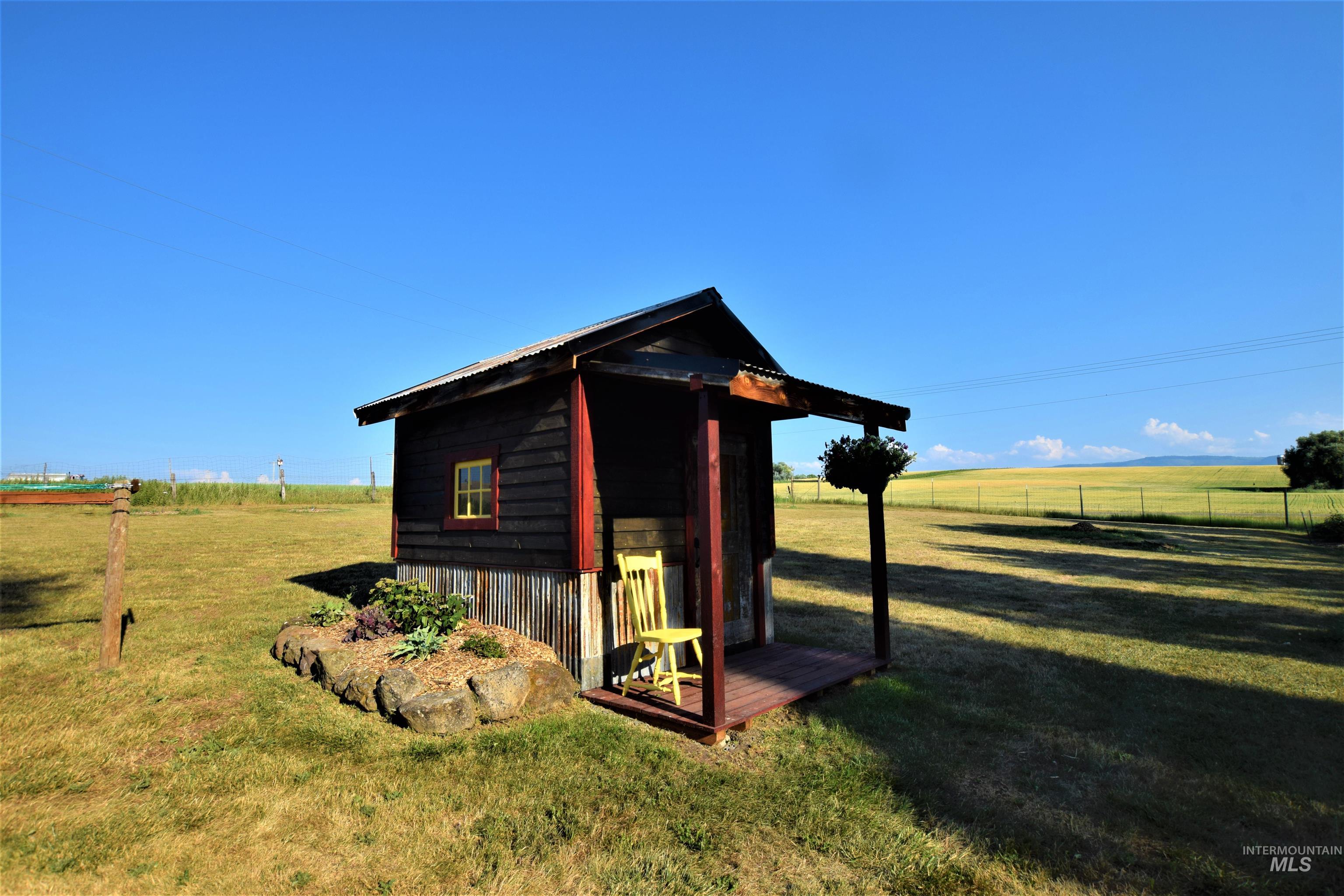 67 Jessup Road Grangeville, ID 83530 - Photo 47 of 49 Wood-sided outbuilding with a corrugated metal roof, featuring a small window with yellow trim, a covered porch, and a rock-edged planting bed