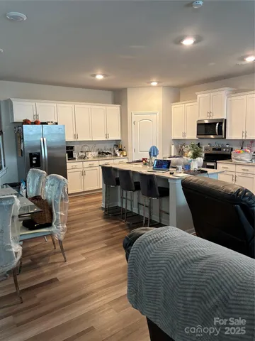 a room with a couch a dining table wooden floor and a view of kitchen
