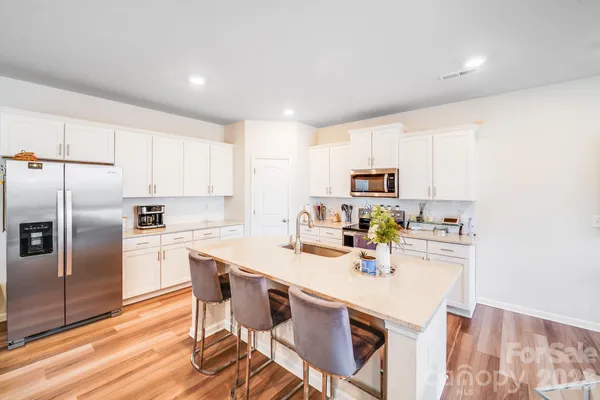 a kitchen with stainless steel appliances a sink a stove a refrigerator cabinets and a dining table with wooden floor