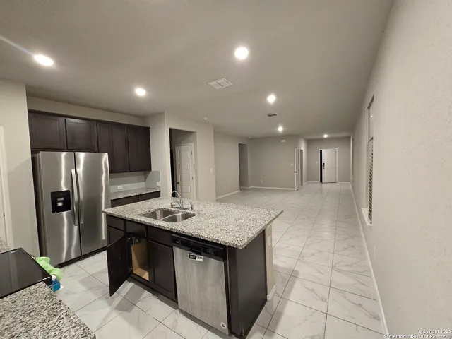 a kitchen with stainless steel appliances kitchen island granite countertop a refrigerator a sink a stove a dining table and chairs