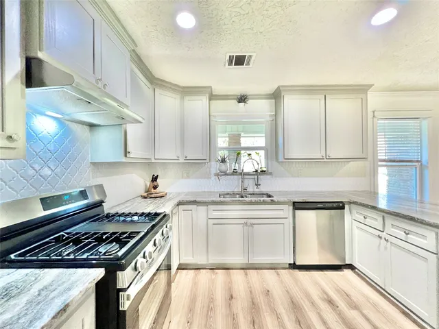 a kitchen with stainless steel appliances granite countertop a stove a sink dishwasher and white cabinets with wooden floor