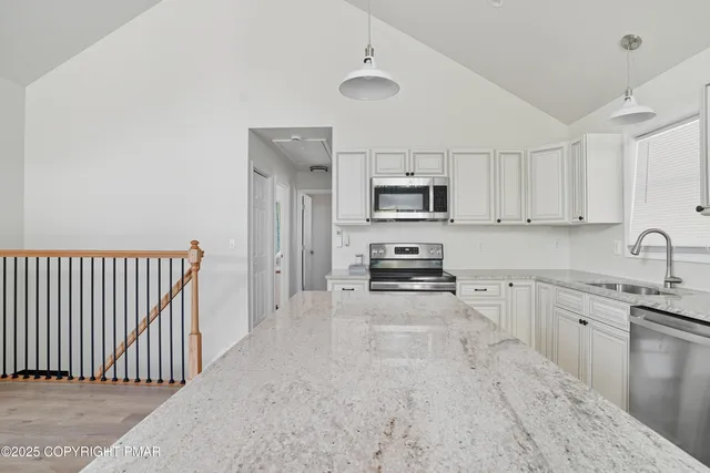 a kitchen with stainless steel appliances a sink a stove a microwave a refrigerator a white cabinets and wooden floor