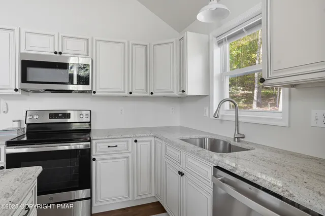 a kitchen with granite countertop a sink cabinets stainless steel appliances and a window