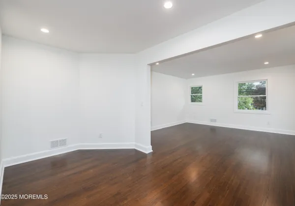 a view of a kitchen and an empty room with wooden floor and a window