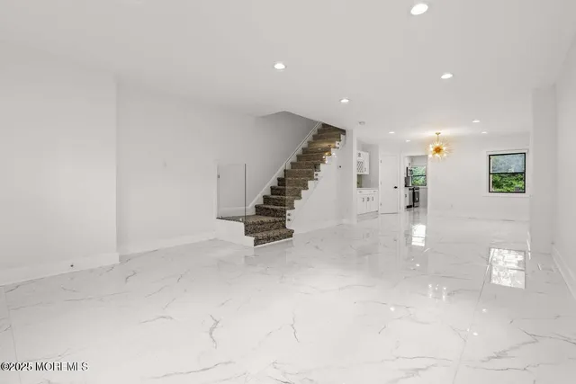 a view of an empty room with chandelier fan and kitchen view