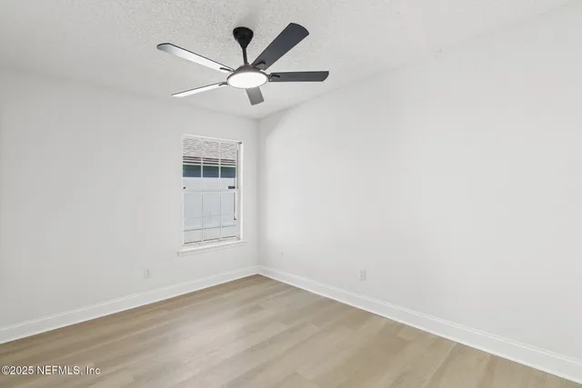 an empty room with wooden floor ceiling fan and window