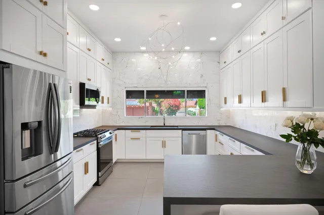 a kitchen with stainless steel appliances kitchen island granite countertop a refrigerator a sink and white cabinets