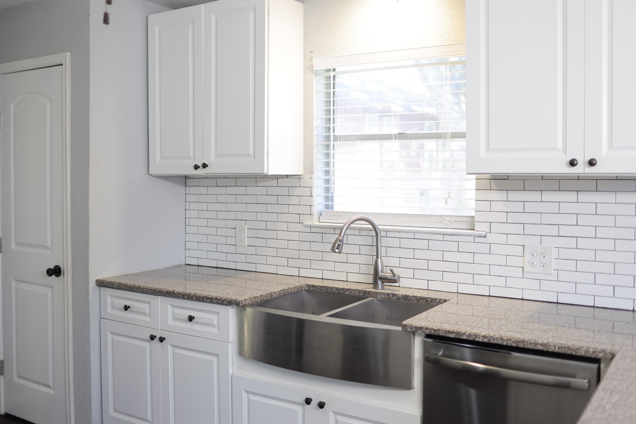 407 Tamarind Street Lake Jackson, TX 77566 - Photo 12 of 36 This kitchen features modern white cabinetry, a sleek stainless steel farmhouse sink, and a stylish subway tile backsplash, creating a clean and inviting space.