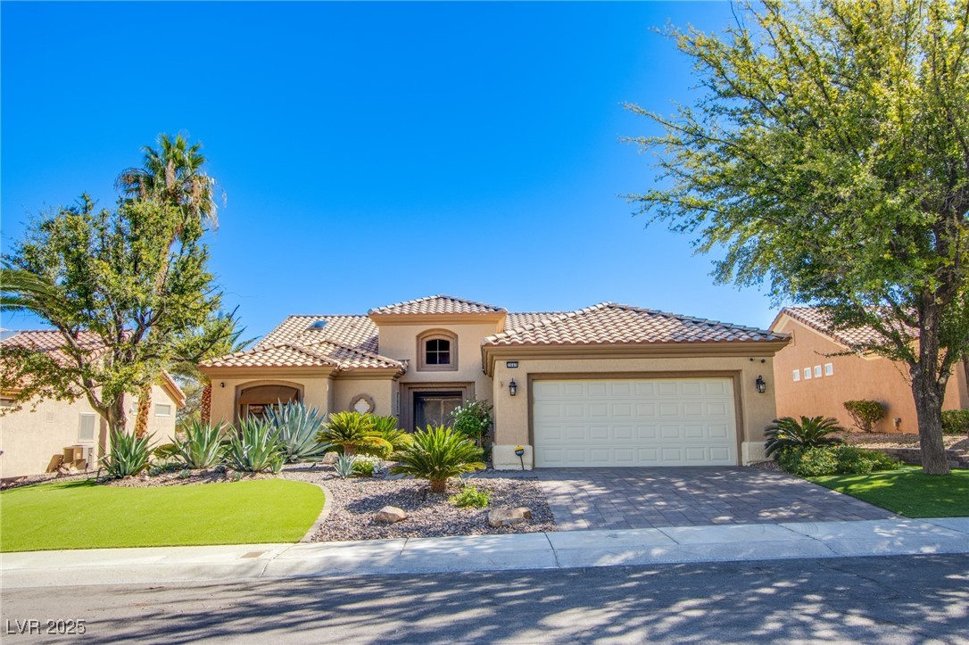 Mediterranean / spanish home featuring stucco siding, decorative driveway, a tiled roof, a garage, and a front yard