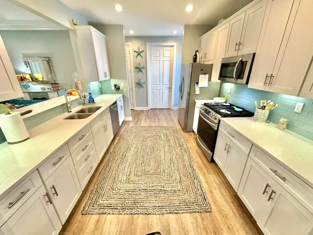 a kitchen with stainless steel appliances a refrigerator a sink a stove a washer dryer and white cabinets