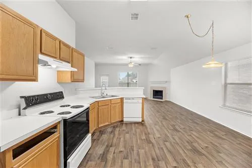 a kitchen with granite countertop a stove top oven a sink dishwasher and white cabinets with wooden floor