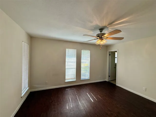 an empty room with wooden floor fan and windows