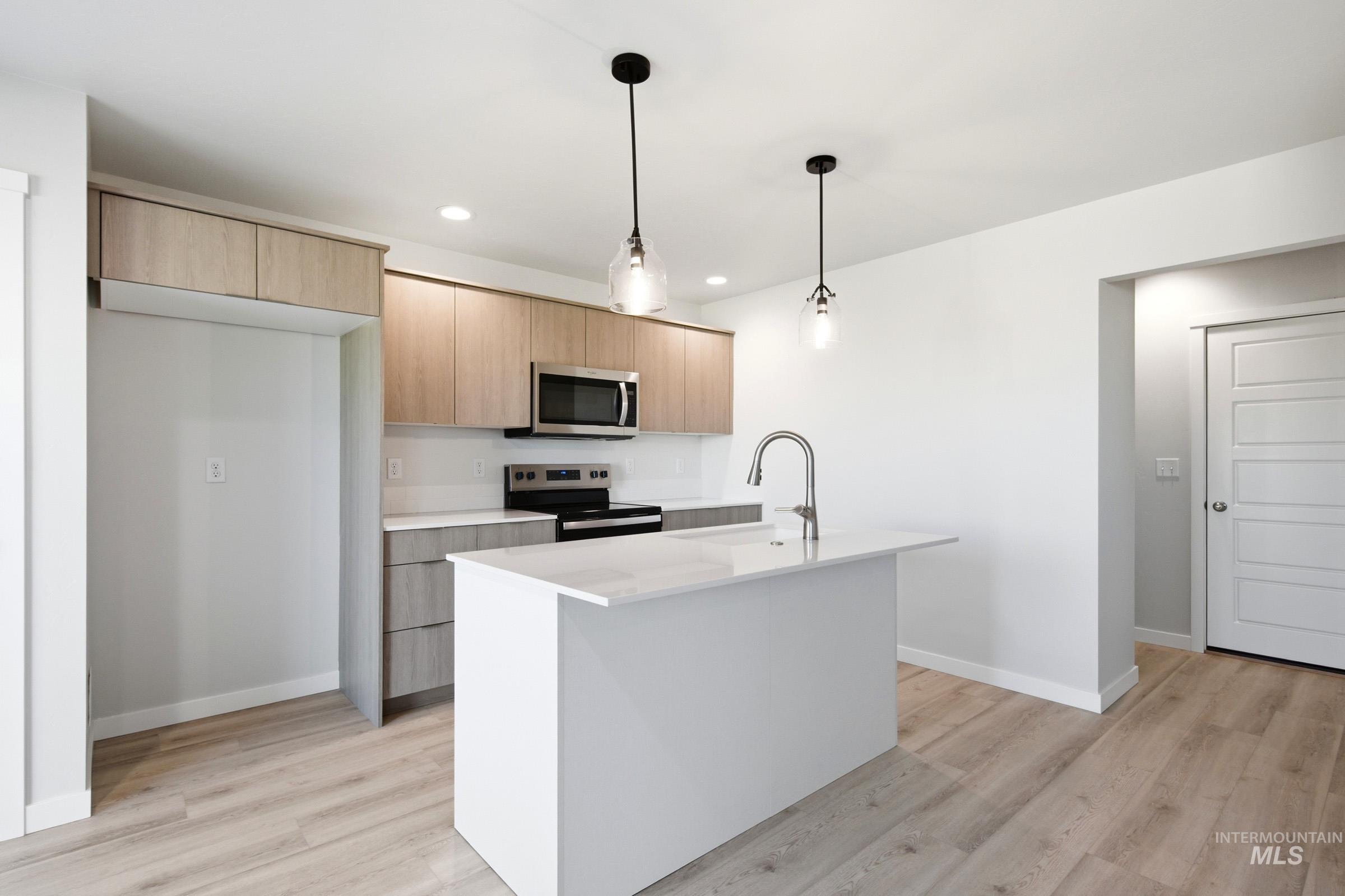 10800 Rutland Street Caldwell, ID 83605 - Photo 3 of 21 Modern kitchen featuring an island with a gooseneck faucet, light wood-finish cabinetry, stainless steel appliances, and wood-finish flooring
