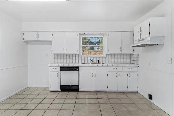 a kitchen with white cabinets appliances a sink and a window