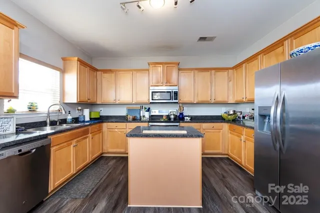 a kitchen with stainless steel appliances granite countertop a stove top oven a sink dishwasher a refrigerator and cabinets with wooden floor