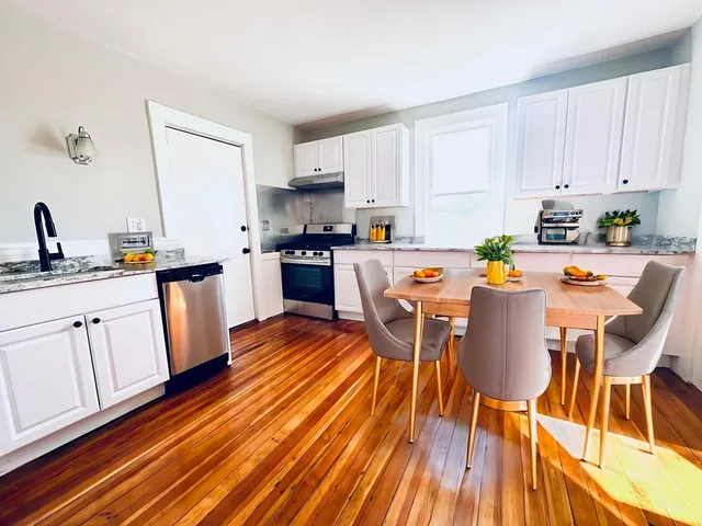 a kitchen with stainless steel appliances granite countertop a stove top oven a sink dishwasher and white cabinets with wooden floor