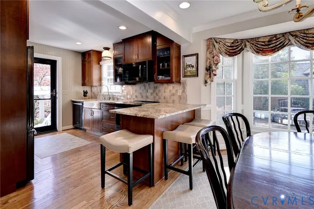 a dinning room with stainless steel appliances kitchen island granite countertop a table chairs and a wooden floor