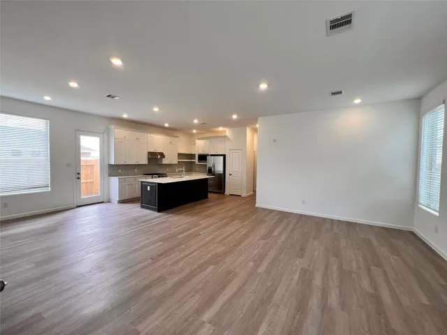 an empty room with wooden floor kitchen view and a window