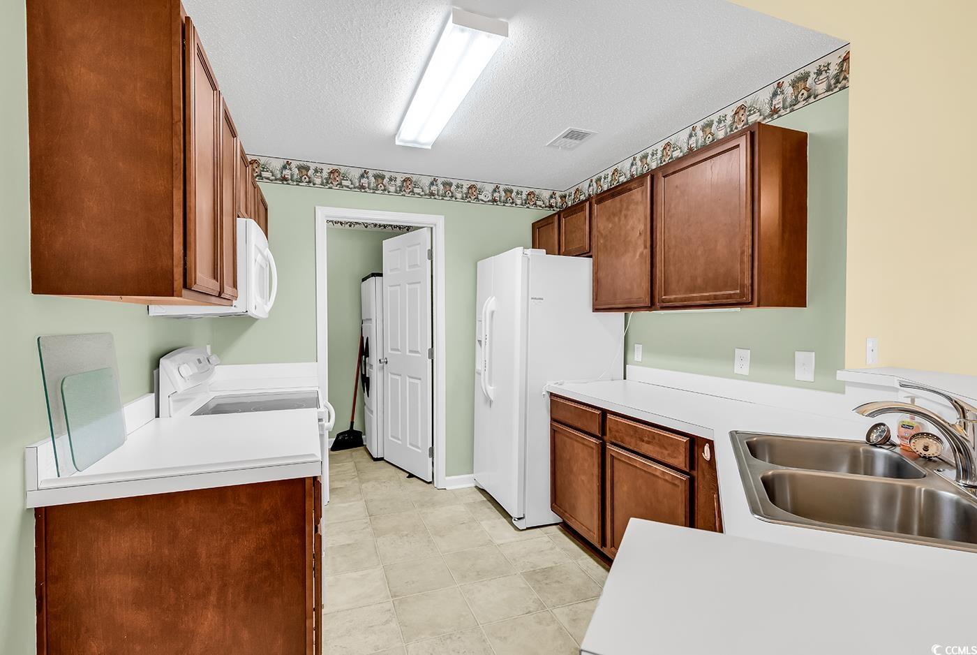 4909 Britewater Court, Unit 202 Myrtle Beach, SC 29579 - Photo 8 of 38 Kitchen featuring brown cabinets, light countertops, white appliances, a textured ceiling, and light tile patterned flooring