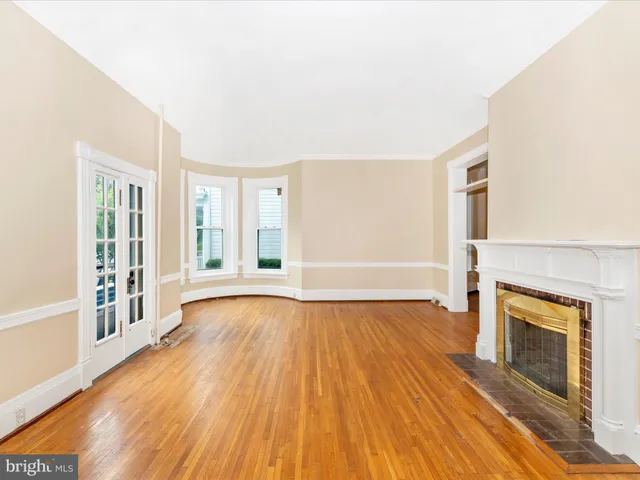 an empty room with wooden floor fireplace and windows