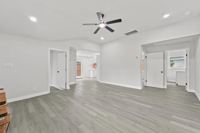 a view of an empty room with wooden floor and a ceiling fan