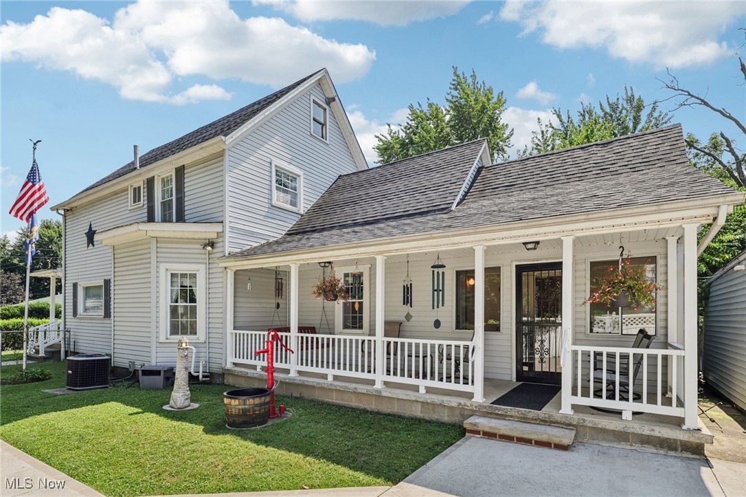 View of front facade with a porch, a shingled roof, and a front yard