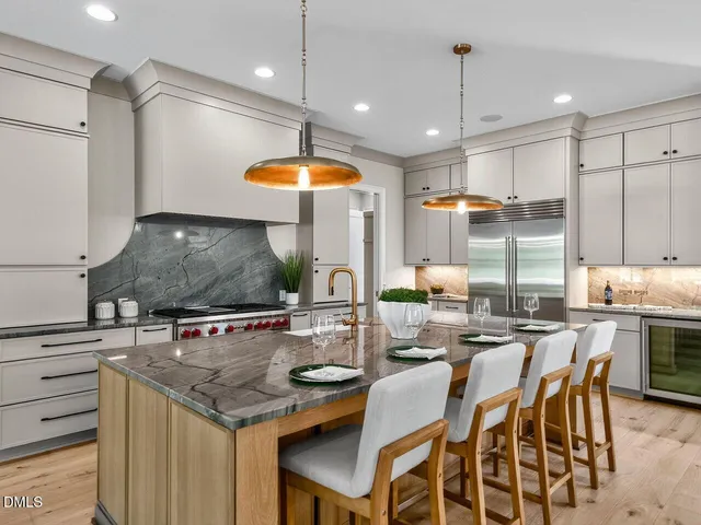 a kitchen with stainless steel appliances granite countertop a stove a refrigerator and a dining table with white cabinets