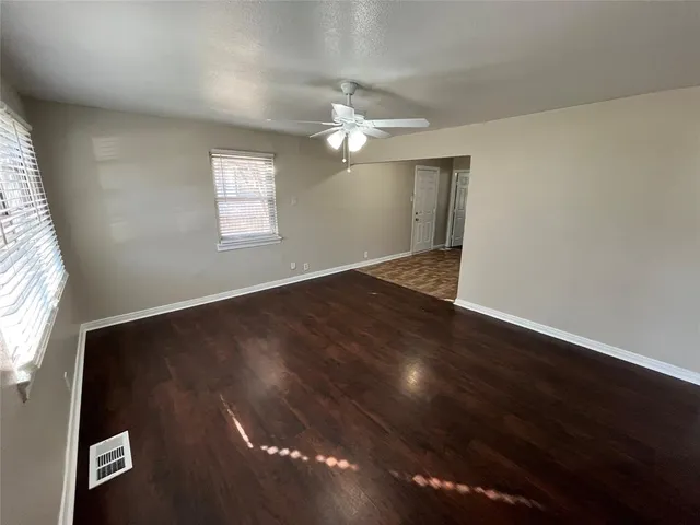 an empty room with wooden floor chandelier fan and windows