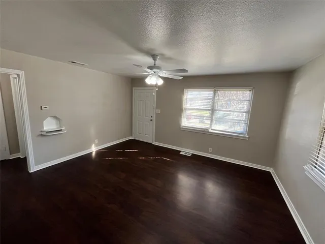 an empty room with wooden floor chandelier fan and windows