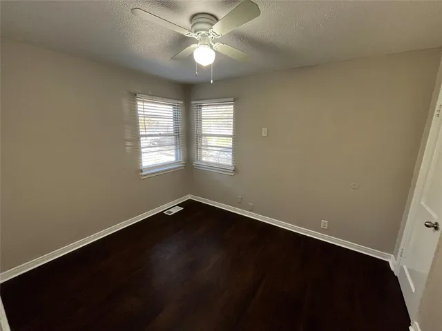 an empty room with wooden floor fan and windows