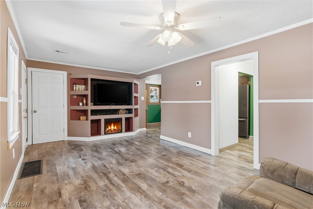 6291 Downs Road Northwest Warren, OH 44481 - Photo 10 of 44 Unfurnished living room with ornamental molding, ceiling fan, light wood finished floors, and a warm lit fireplace