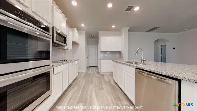 a kitchen with a sink dishwasher a stove and white cabinets with wooden floor