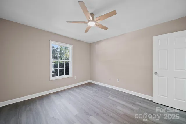 an empty room with wooden floor fan and windows