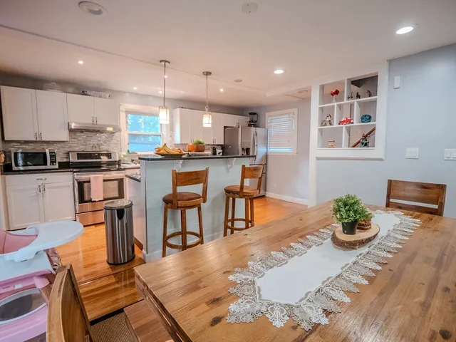 a kitchen with stainless steel appliances granite countertop a refrigerator a stove top oven a dining table and chairs with wooden floor