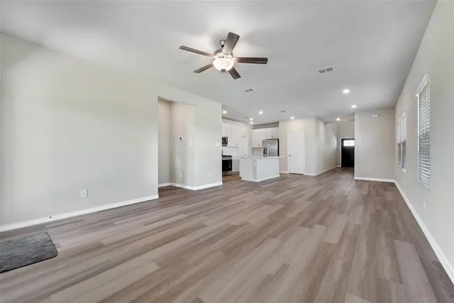 a view of an empty room with wooden floor and a ceiling fan