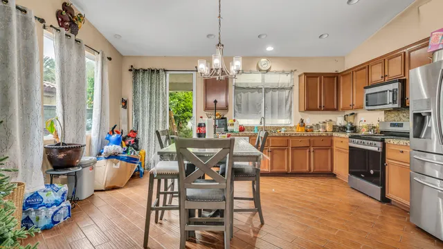 a kitchen with stainless steel appliances kitchen island granite countertop a stove top oven a sink a dining table and chairs with wooden floor