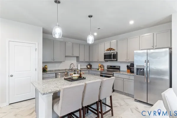 a kitchen with stainless steel appliances granite countertop a refrigerator a stove a sink a center island a dining table and chairs