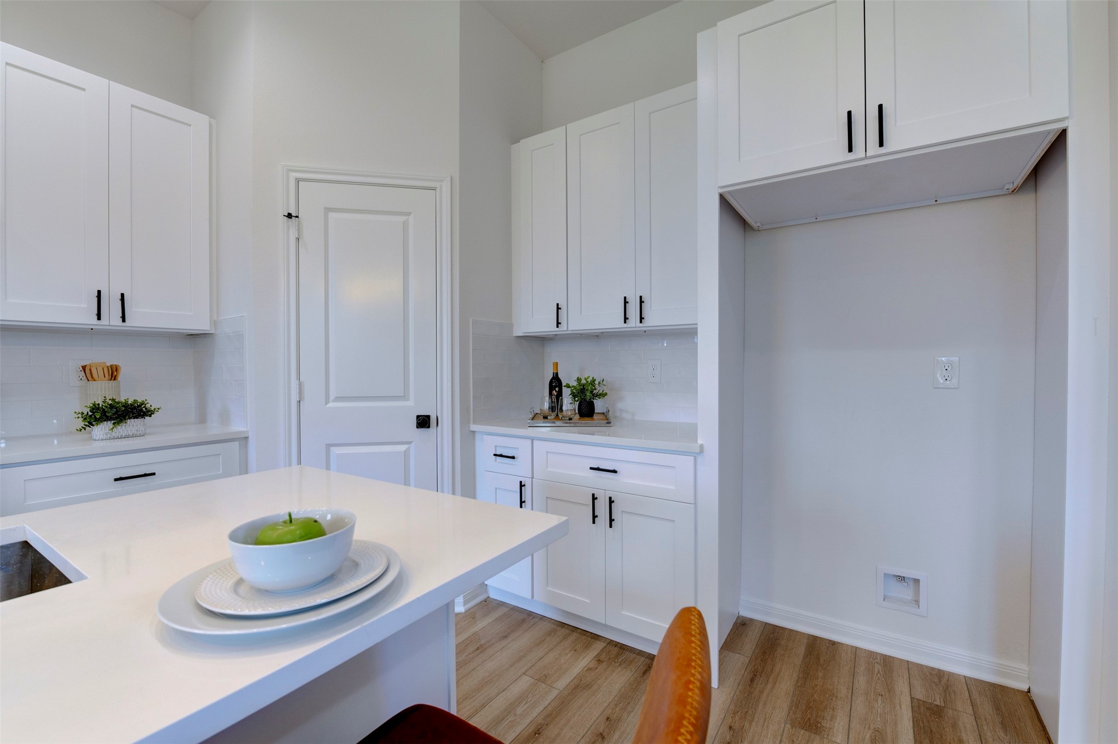 6807 Paris Street Houston, TX 77021 - Photo 24 of 50 Kitchen storage wall showing floor-to-ceiling white shaker cabinets with matte black hardware, quartz countertop, subway tile backsplash, pantry door, and open appliance niche with overhead cabinet.